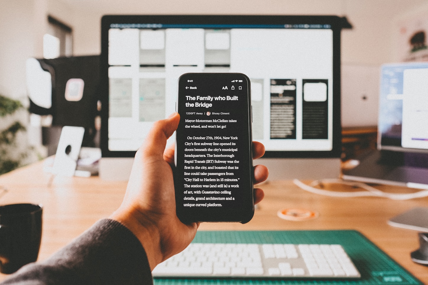 Hand holding a smartphone in front of a development workspace